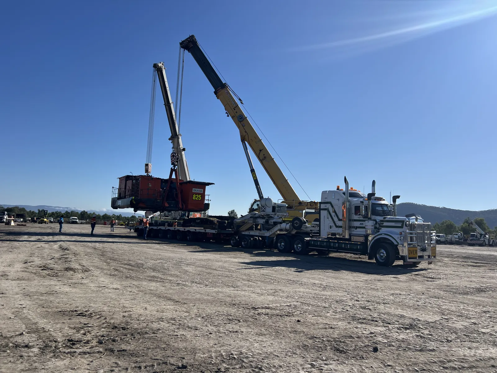 Cranes lifting a heavy component onto a low loader
