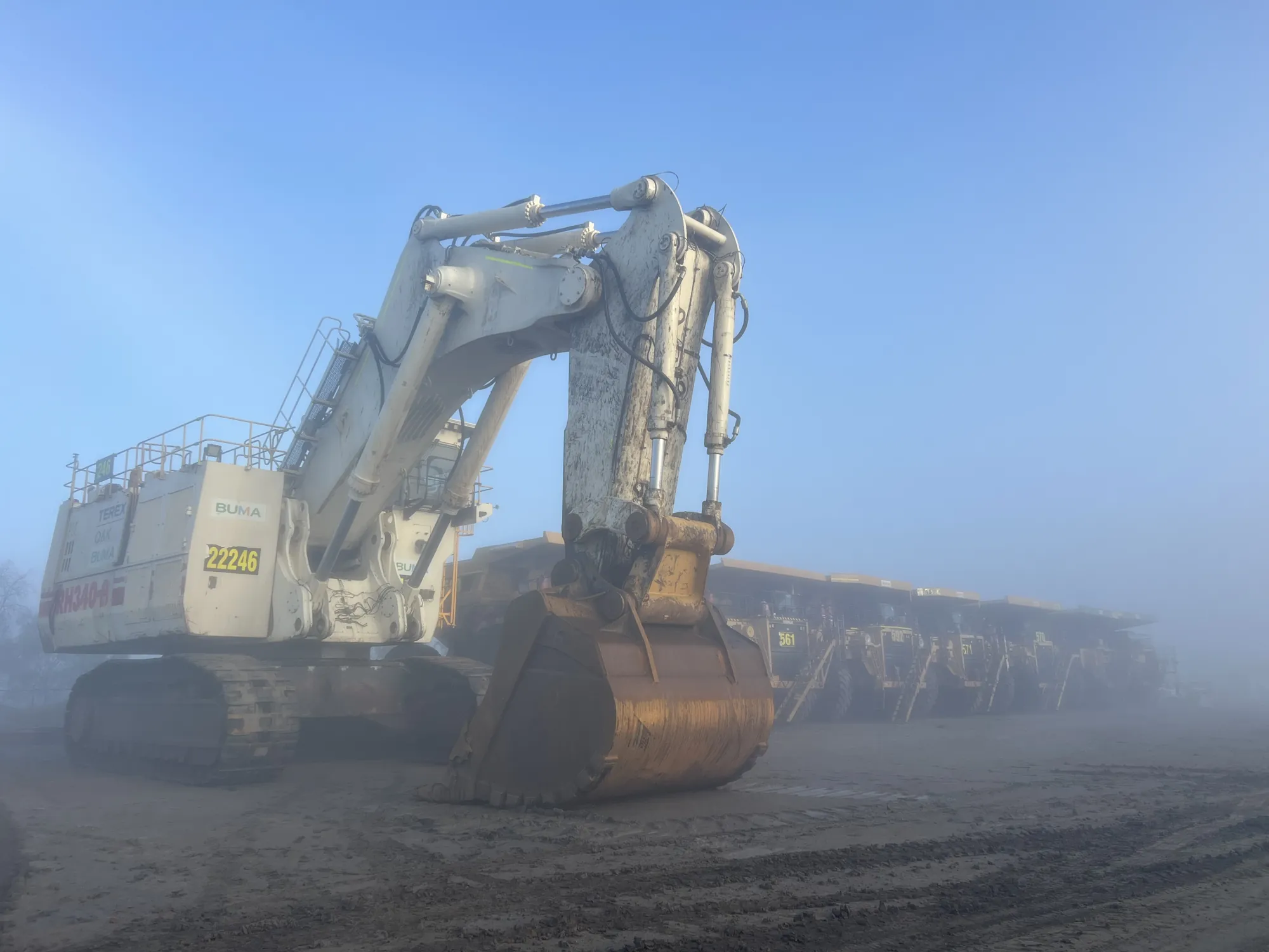 Excavator and haul trucks in morning fog